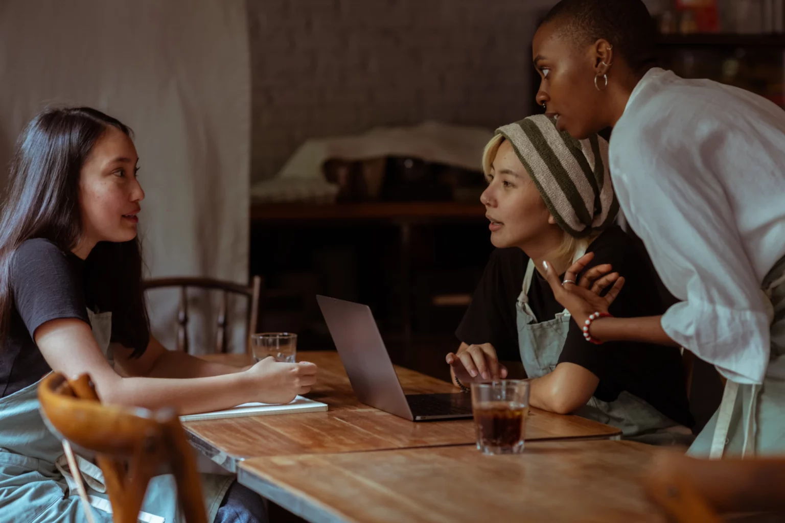 Three colleagues collaborating around a laptop at a wooden table